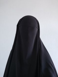 a woman wearing a black hijab is standing in front of a white wall