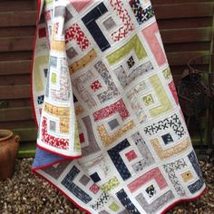 a patchwork quilt is hanging on the side of a building in front of a potted plant