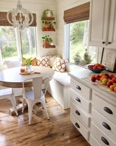 a kitchen filled with lots of counter space and white cabinets next to a table topped with fruit