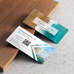 two business cards sitting next to each other on top of a wooden table with white and blue designs