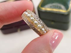 a close up of a person's hand holding a ring with pearls on it