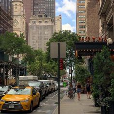 cars parked on the street in front of tall buildings and people walking down the sidewalk