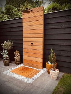 an outdoor shower in the middle of a garden with potted plants and rocks on the ground