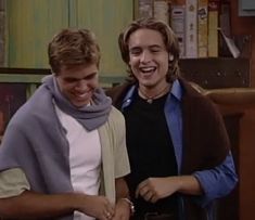 two people standing next to each other in front of a bookshelf and smiling