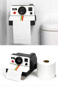 a polaroid camera sitting on top of a roll of toilet paper next to a white toilet