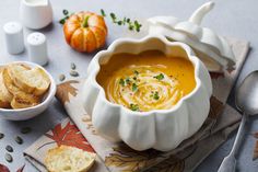 a white bowl filled with soup next to crackers and pumpkins on a table