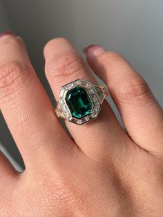 a woman's hand with a ring on it and an emerald stone in the middle