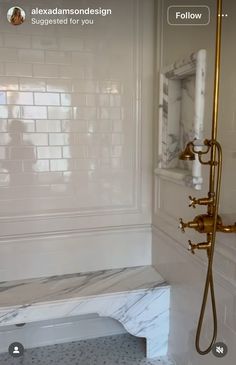 a bathroom with white tile and gold fixtures on the shower wall, along with a marble bench