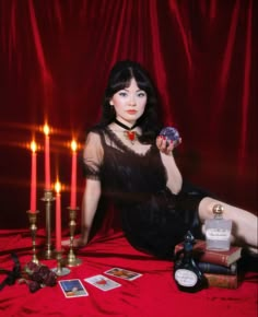 a woman sitting in front of candles with cards on the floor next to her and holding a ball