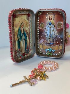 an open box with two pictures and a key on the table next to some beads