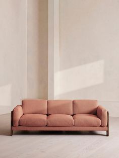 a pink couch sitting on top of a hard wood floor next to a white wall