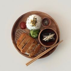 a wooden plate topped with meat and rice next to chopsticks on a table