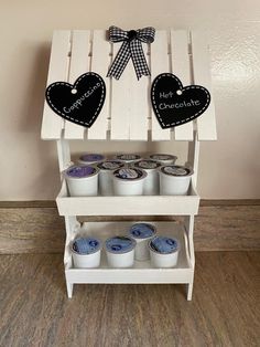 a wooden shelf with cupcakes on it and two hearts hanging from the top