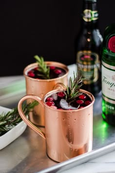 two copper mugs filled with cranberry punch and rosemary garnishes