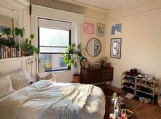 a bedroom with a bed, bookshelf and various items on the floor in front of a window