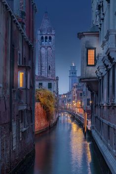 a river running through a city with tall buildings on both sides and a clock tower in the distance