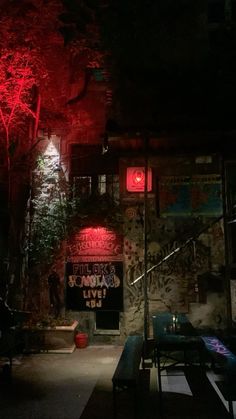 a red light shines on the side of a brick building with graffiti and trees