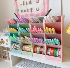 a desk with many different types of pens and pencils in containers next to a keyboard