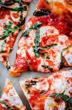 several slices of pizza with cheese, spinach and other toppings on a sheet of parchment paper