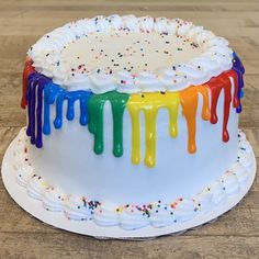 a cake with white frosting and multicolored icing on it sitting on a wooden table