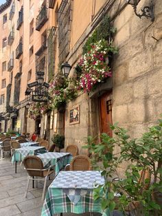 tables and chairs are lined up on the side of an alleyway with flowers hanging over them