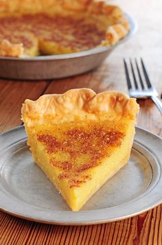 a slice of quiche on a plate next to a pie pan with a fork