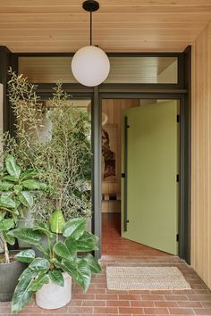 a house with green doors and plants in the entryway, on brick flooring