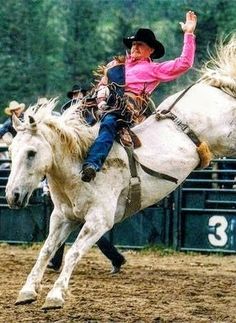 a woman in pink shirt riding on the back of a white horse at a rodeo