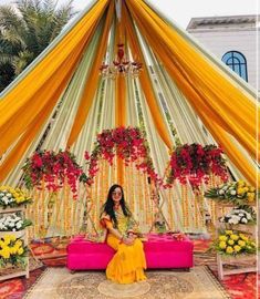 a woman sitting on top of a pink couch under a yellow and red canopy covered in flowers