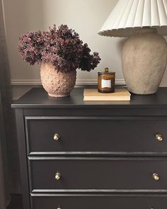 a vase with flowers on top of a black dresser next to a book and lamp