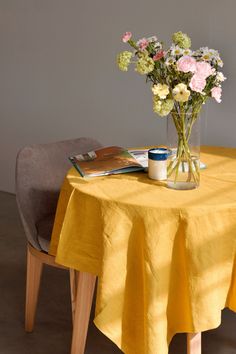 a vase with flowers sitting on top of a yellow table cloth next to a book