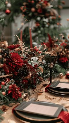 the table is set for christmas dinner with red flowers and greenery on each plate