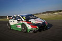 a green and white car driving on a race track with blue sky in the background