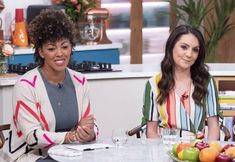 two women sitting at a table with fruit on it