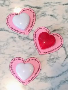 three pink and white heart shaped magnets with words on them sitting on a marble surface