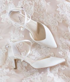 two pairs of white shoes sitting on top of a lace covered table cloth next to each other