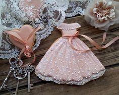 there is a pink dress and keys on the table next to lace doily with flowers