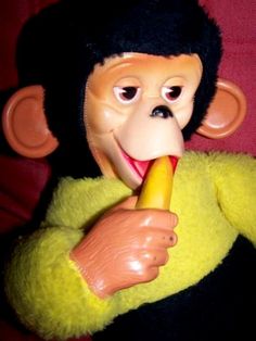 a toy monkey holding a banana in its mouth and wearing a yellow shirt with black hair