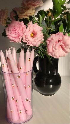 pink flowers and candles in a vase on a white table with black vase behind them