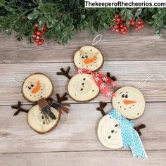 three snowmen made out of wood slices on top of a wooden table next to evergreen branches