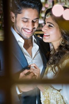 a man and woman standing next to each other in front of a mirror with lights behind them