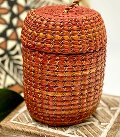 an orange woven basket sitting on top of a wooden table next to a leafy plant