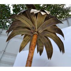 a large metal palm tree next to a white wall and trees in the back ground