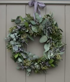 a wreath hanging on the side of a building with greenery and lavenders around it