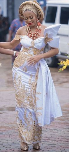 a woman in a white and gold dress is walking down the street with her hand on her hip