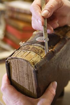 a person holding a pair of scissors over an old book that is being held by someone's hands