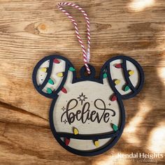 a mickey mouse ornament hanging on a wooden surface with lights and the words believe