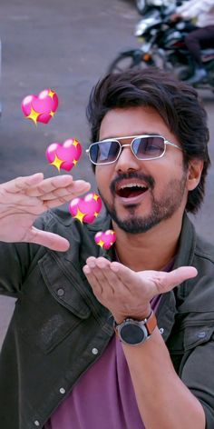 a man wearing sunglasses and pointing to pink hearts on his fingers in front of him