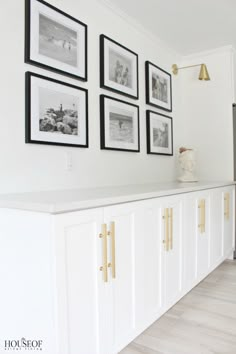 a kitchen with white cabinets and framed pictures on the wall above it, along with gold handles