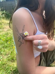 a woman with a tiny daisy tattoo on her left arm and right hand, sitting in the grass